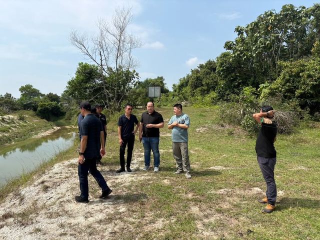 The team stands on a sandy bank beside the water