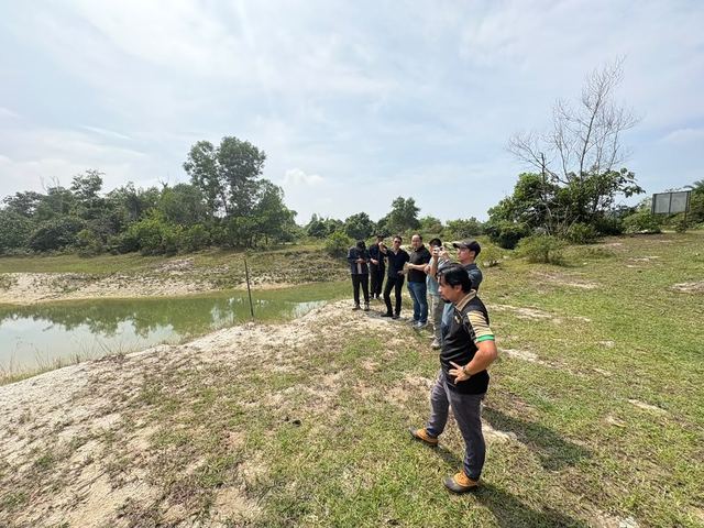The team walks along the raised bank beside the lake